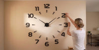 Horloge murale géante 3D adhésive noire pour salon, avec chiffres DIY collés sur le mur par une femme blonde