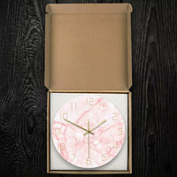 Horloge murale ronde marbre rose et or emballée dans sa boîte de rangement en carton sur fond de bois sombre.
