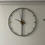 Horloge murale decorative salon  en métal noir et détails dorés fixée sur un mur blanc.