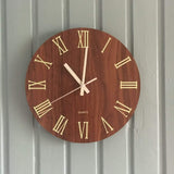 Photo client d'une horloge murale moderne chiffre romain installée sur un mur en lambris gris.