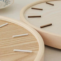 Gros plan sur les finitions du cadran et les index en relief d'une pendule murale silencieuse en bois naturel.