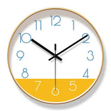Horloge murale nordique au design scandinave, avec cadran blanc et partie inférieure jaune moutarde. Les aiguilles noires contrastent avec les chiffres bleus. Son contour peut être noir ou doré. Cette horloge murale moderne et élégante apporte une touche chaleureuse et originale à un salon, une chambre ou un bureau doré cadran