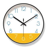 Horloge murale nordique au design scandinave, avec cadran blanc et partie inférieure jaune moutarde. Les aiguilles noires contrastent avec les chiffres bleus. Son contour peut être noir ou doré. Cette horloge murale moderne et élégante apporte une touche chaleureuse et originale à un salon, une chambre ou un bureau