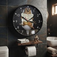 une horloge murale décorative, intitulée "Cat News," qui montre un chat tigré assis sur des toilettes, lisant un journal. L'horloge est positionnée au-dessus d'un support en bois qui comprend des journaux pliés, un petit chat miniature lisant un livre et un rouleau de papier toilette avec des motifs de pattes de chat. La scène est dans une salle de bain avec des carreaux muraux sombres.