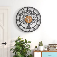 Grande horloge murale design Arbre de Vie en métal et bois accrochée sur un mur blanc au-dessus d'une commode et de plantes