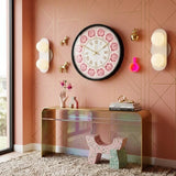 Horloge murale kitsch à bordure noire et cadran à motif de roses roses romantiques avec aiguilles dorées, fixée sur un mur rose géométrique style piece shabby rosé