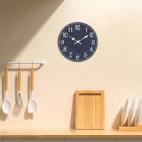 Horloge murale bleue marine ancienne accrochée au-dessus d'un plan de travail de cuisine clair avec ustensiles en bois.