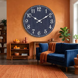 Horloge murale bleue marine ancienne accrochée dans une salle à manger moderne au mur bleu foncé avec luminaires en cuivre.