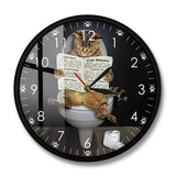 l'horloge murale ronde au cadran noir. L'image met en avant le motif central : un chat tigré assis sur la cuvette des toilettes, lisant un journal intitulé « Cat News » avec des rubriques comme « Sports News » ou « Political life ». Le cadran comporte des chiffres blancs épurés et des petites pattes de chat à la place des index des heures