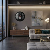 Cette image montre un salon contemporain, lumineux grâce à une grande baie vitrée, décoré avec une horloge murale originale en forme de compteur de vitesse noir, placée au-dessus d'un buffet en bois.