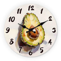 Horloge murale cuisine représentant un demi-avocat coupé avec son noyau brun au centre et sa chair verte détaillée avec un effet peinture artistique sur un cadran beige clair, accompagnée de chiffres noirs lisibles pour une décoration murale originale.