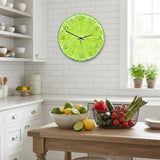 Horloge murale ronde design en forme de tranche de citron vert éclatante, accrochée sur un mur en carrelage blanc dans une cuisine moderne et lumineuse.