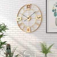 Horloge murale dorée design accrochée sur un mur parement en briques blanches lumineuses. Le mélange des chiffres mixtes et des plantes vertes environnantes apporte une atmosphère chaleureuse et tendance à votre intérieur.