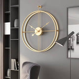 Horloge murale dorée design exposée sur un mur gris foncé sophistiqué. La proximité d'une lampe articulée noire met en valeur les reflets chaleureux de la couleur or.