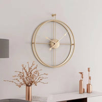 Horloge murale dorée design suspendue au-dessus d'une console élégante en arrière-plan. L'association avec un vase fleuri et des bougeoirs dorés crée une décoration d'intérieur raffinée.