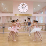 L'horloge murale thème ballerine est accrochée au mur d'un studio de danse classique au-dessus d'un grand miroir. Au premier plan, de jeunes danseurs en tutu rose et tenues de ballets répètent au centre de la salle au parquet clair