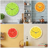 quatre images montrant des horloges murales rondes et design ayant l'apparence de tranches de fruits frais : une lime verte, une orange sanguine, une pastèque rouge et un citron jaune, installées dans des décors de cuisines modernes et lumineuses.