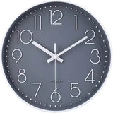 Une horloge murale grise pour cuisine au design classique. Elle présente un cadran gris anthracite uni, des chiffres arabes blancs fins et arrondis, et un index des minutes sous forme de petits points blancs.