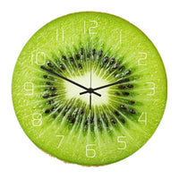 une horloge murale ronde au motif réaliste de tranche de kiwi. Le fond présente la chair verte acidulée et les petits pépins noirs du fruit, avec des chiffres blancs épurés et des aiguilles noires au centre