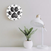 Horloge murale patte de chien originale avec une empreinte de patte noire au centre du cadran sur un fond blanc cassé. Les chiffres noirs et les trois aiguilles assorties créent un design épuré et moderne. Une décoration murale idéale pour les amoureux des chiens pour la chambre