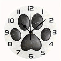 Horloge murale patte de chien originale avec une empreinte de patte noire au centre du cadran sur un fond blanc cassé. Les chiffres noirs et les trois aiguilles assorties créent un design épuré et moderne. Une décoration murale idéale pour les amoureux des chiens