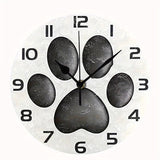 Horloge murale patte de chien originale avec une empreinte de patte noire au centre du cadran sur un fond blanc cassé. Les chiffres noirs et les trois aiguilles assorties créent un design épuré et moderne. Une décoration murale idéale pour les amoureux des chiens