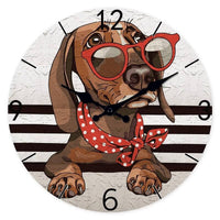 Horloge murale teckel représentant un adorable chien couché avec la tête posée sur ses deux pattes avant. Le teckel porte de grandes lunettes rouges originales ainsi qu'un foulard rouge à pois blancs qui lui donne un style unique et plein de charme. Son regard doux et attentif semble montrer toute sa tendresse et sa complicité avec son propriétaire. Le cadran blanc gris clair apporte une touche élégante tandis que les quatre bandes noires créent un design moderne qui met en valeur l'illustration du chien. 