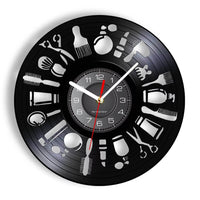 Horloge murale ronde en vinyle noir avec pictogrammes blancs d'outils de barbier comme le blaireau, les ciseaux, le rasoir et le peigne sur le cadran.