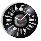 Horloge murale ronde en vinyle noir avec pictogrammes blancs d'outils de barbier comme le blaireau, les ciseaux, le rasoir et le peigne sur le cadran.