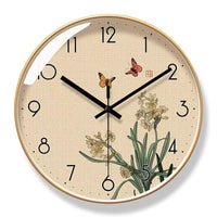 Horloge murale design style asiatique avec cadre doré. Cadran effet toile beige orné d'une illustration d'inspiration japonaise avec des jonquilles jaunes, deux papillons orange et un sceau rouge traditionnel