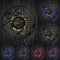 Avec LED - Horloge murale en vinyle noir représentant un skateur réalisant une figure avec sa planche de skateboard devant un décor de bâtiments urbains, avec cadran central et aiguilles noires et rouges.