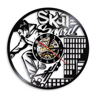 Horloge murale en vinyle noir représentant un skateur en plein saut avec sa planche de skateboard, entouré d'éléments graphiques urbains.
