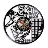 Horloge murale en vinyle noir représentant un skateur en plein saut avec sa planche de skateboard, entouré d'éléments graphiques urbains.