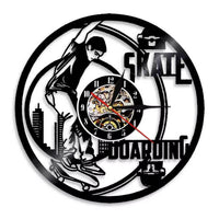 Horloge murale en vinyle noir représentant un skateur réalisant une figure avec sa planche de skateboard devant un décor de bâtiments urbains, avec cadran central et aiguilles noires et rouges.