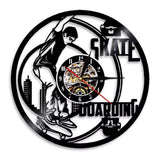 Horloge murale en vinyle noir représentant un skateur réalisant une figure avec sa planche de skateboard devant un décor de bâtiments urbains, avec cadran central et aiguilles noires et rouges.
