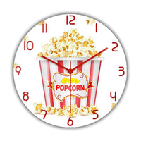 Horloge murale Popcorn originale avec un pot rouge et blanc rempli de popcorn. Plusieurs popcorns débordent du pot et certains sont tombés autour. Les chiffres et les aiguilles rouges rappellent l’ambiance des salles de cinéma. Cette décoration murale apporte une touche ludique et conviviale à votre intérieur et salon.