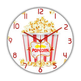 Horloge murale Popcorn originale avec un pot rouge et blanc rempli de popcorn. Plusieurs popcorns débordent du pot et certains sont tombés autour. Les chiffres et les aiguilles rouges rappellent l’ambiance des salles de cinéma. Cette décoration murale apporte une touche ludique et conviviale à votre intérieur et salon.