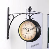 L'horloge murale double face de style vintage, avec son support en métal noir, est fixée à un mur blanc. En arrière-plan, sur la droite, un grand cadre noir contient une affiche avec le mot "tomorrow" en noir. Le cadran de l'horloge est crème vieilli avec des chiffres arabes noirs et le texte "GRAND CENTRAL TERMINAL - NEW YORK".