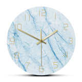 Horloge murale ronde effet marbre bleu veiné avec chiffres arabes fins et aiguilles dorées.