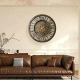 Horloge murale style industrielle rétro avec chiffres romains et engrenages apparents accrochée au mur d'un salon au-dessus d'un canapé en cuir