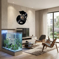 L'horloge murale vinyle est exposée dans un grand salon moderne et lumineux. Elle est placée au-dessus d'un meuble TV, à côté d'un grand aquarium lumineux contenant de nombreux poissons et plantes aquatiques. Deux chaises design en bois et cuir complètent le décor épuré.