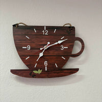 Avis client en photo réelle d'une pendule murale en bois foncé en forme de tasse de café accrochée sur un mur blanc