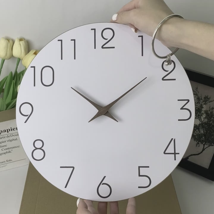 Vidéo de présentation d'une horloge murale design blanche avec des aiguilles en bois naturel, illustrant son style minimaliste et son mouvement fluide.