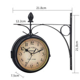 horloge murale double face de style vintage avec son support en métal noir, fixée sur un fond blanc uni. Des lignes de cote blanches avec des mesures en centimètres sont superposées à l'image pour indiquer les dimensions de l'horloge : 21.8cm pour la hauteur et la largeur du support, et 7.5cm pour l'épaisseur du cadran. Le cadran crème vieilli, les chiffres noirs et le texte "GRAND CENTRAL TERMINAL - NEW YORK" sont visibles.