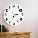 Horloge inversée ronde 30 cm blanche design antihoraire accrochée au-dessus d'une commode en bois dans une chambre