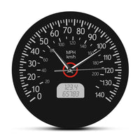 Horloge murale ronde au design de compteur de vitesse automobile, dotée d'un fond noir mat, de chiffres et graduations blancs allant de 0 à 140, des mentions « MPH » et « km/h », d'un faux écran numérique à cristaux liquides affichant des chiffres gris, ainsi que d'aiguilles blanches et d'un axe central cerclé de rouge.