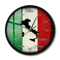 Vue de face d'une horloge murale ronde avec un cadre noir, posée sur un fond blanc avec une ombre portée. Le cadran présente le drapeau italien, la carte noire de l'Italie et les heures écrites en toutes lettres en italien.