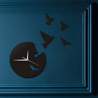 Horloge murale originale design noire sans chiffres avec découpe d'oiseaux s'envolant et aiguilles blanches sur un mur salon bleu