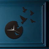 Horloge murale originale design noire sans chiffres avec découpe d'oiseaux s'envolant et aiguilles blanches sur un mur salon bleu