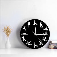 Horloge murale position sexuelle Kama Sutra noire avec silhouettes et aiguilles blanches, posée comme objet de décoration sur une table basse dans un salon moderne.